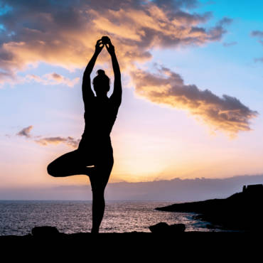 Silhouette of a woman doing yoga stretches on the beach during sunset